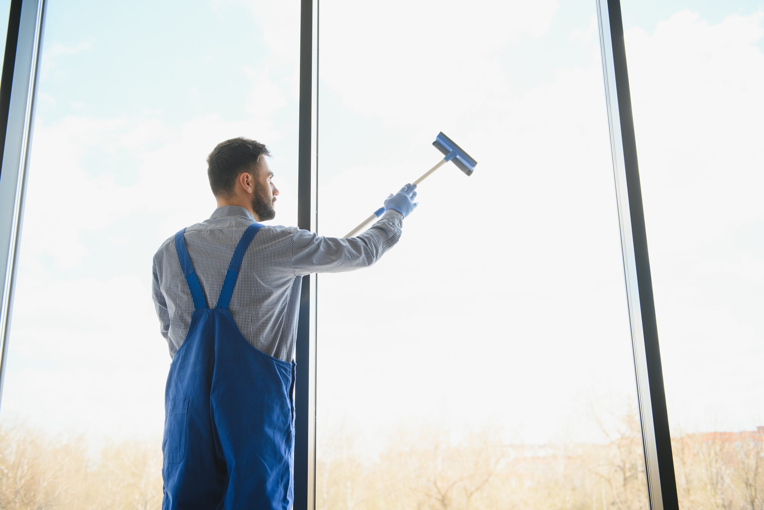 Male janitor cleaning window in office.