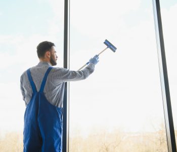 Male janitor cleaning window in office.